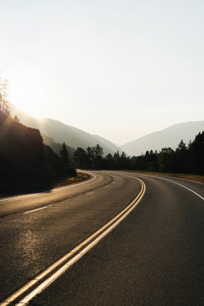 Dağ yolunda gün doğumu — virajlı asfalt yol ve uzak dağ silueti.